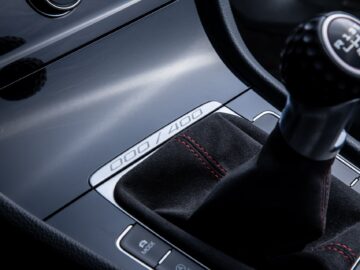 Close-up of a manual car gearshift with stitching and buttons on a sleek black console, with the numbers 000/400. Perfect for any Golf enthusiast or motorsports enthusiast.