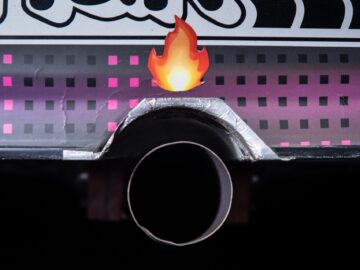 Close-up of a vehicle's exhaust pipe decorated with a flame sticker and patterned design with pink squares, capturing the essence of motorsport style in vivid detail.