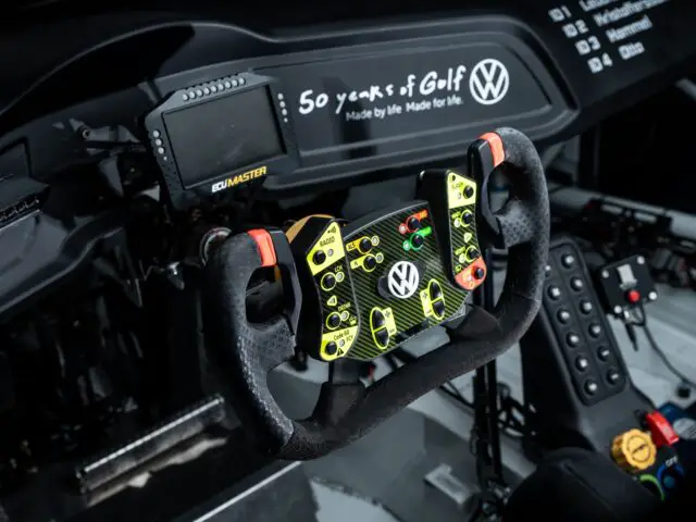 Close-up of a car's racing cockpit with a complex steering wheel with various knobs and paddles, a small monitor and Volkswagen's 