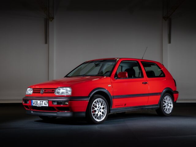 A red Volkswagen Golf GTI, with three doors, is parked inside. The car features silver alloy wheels and a rear antenna.