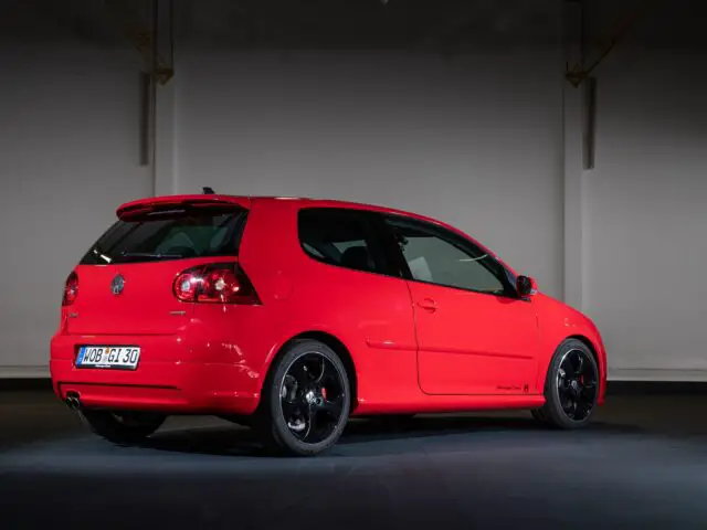 A red two-door Volkswagen Golf GTI hatchback is parked inside, showing its rear and side profile. The car has tinted windows, black alloy wheels and a visible European license plate.