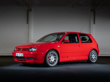 A red Volkswagen Golf GTI is parked inside under direct light, elegantly displaying its sleek design and alloy wheels.