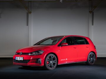A red Volkswagen Golf GTI is parked inside against a dark background. This sleek car features black alloy wheels and a front license plate that reads 