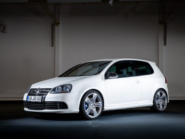 A Volkswagen Golf GTI, white and compact with alloy wheels, is parked in a poorly lit interior environment, seen from a three-quarter forward angle.