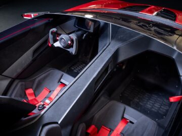 Red-black sports car interior with two seats with red seat belts, a steering wheel with a digital display behind it and a minimalist dashboard design reminiscent of a modern Volkswagen Golf.