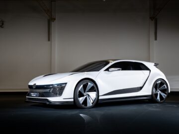 In a showroom with a dark floor and minimal background, a futuristic white Volkswagen Golf hatchback with a sleek design is on display.