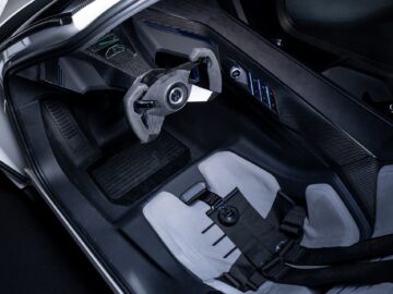 Inside view of a Volkswagen Golf with futuristic steering wheel, racing seat with harness and sleek black and gray design.