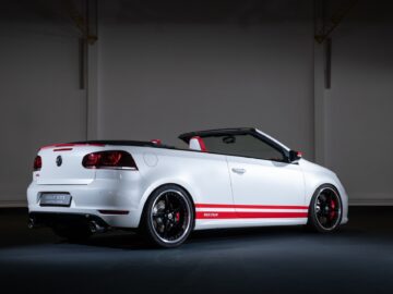 Inside, a white Volkswagen Golf convertible with a black roof and red accents is parked, displaying a sporty design. Red stripe details and black rims are visible.