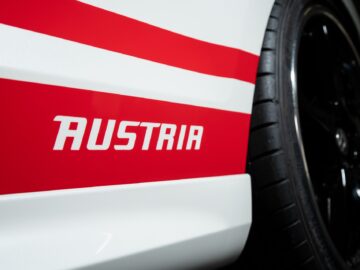 Close-up van een Volkswagen Golf met een rood-wit gestreept ontwerp en het woord "AUSTRIA" vetgedrukt op de zijkant. De afbeelding is scherpgesteld op het onderste gedeelte nabij het wiel.