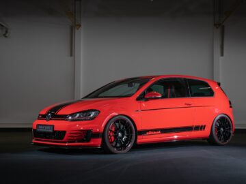 Een rode, sportieve Volkswagen Golf met zwarte racestrepen, zwarte velgen en strakke aerodynamische kenmerken staat geparkeerd in een slecht verlichte garage.