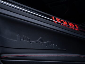 Close-up of the interior door panel of a Volkswagen Golf featuring a sleek black design with red accent stitching and a subtle embossed skyline image.