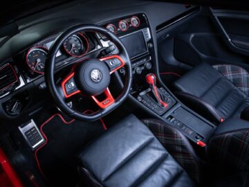 The interior of the Volkswagen Golf features a well-crafted dashboard, steering wheel, gearshift and leather seats with striking red accents and classic checkered patterns.