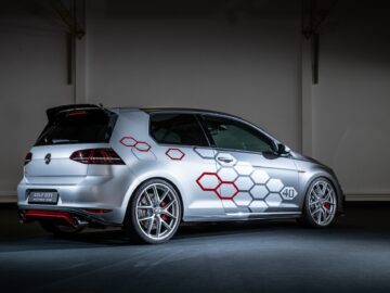 Der silberne Volkswagen Golf GTI 40th Anniversary Edition, mit sechseckigen Emblemen an der Seite und roten Akzenten an den Rädern, wird im Innenraum ausgestellt.