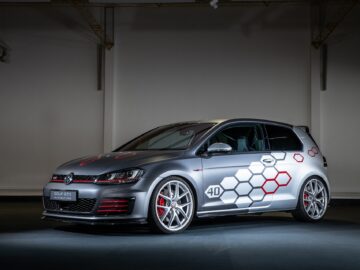 Een zilveren Volkswagen Golf GTI, versierd met zeshoekige emblemen aan de zijkant en '40' op de deur, staat binnen geparkeerd tegen een effen achtergrond.