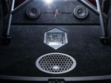 Close-up of the audio system of a Volkswagen Golf with speakers, a subwoofer with honeycomb grille, an illuminated audio control module in the center and a metal support bar at the front.