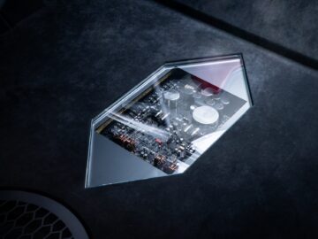 A close-up of electronic circuits visible through a diamond-shaped transparent window in a dark, textured surface, reminiscent of the intricate design elements in a Volkswagen Golf.