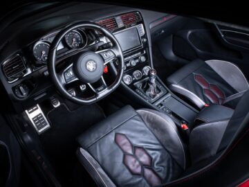 A view from a high angle of the interior of a Volkswagen Golf. The design features a sleek dashboard, leather seats, a manual transmission and a multi-function steering wheel.