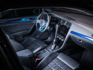 The interior of a modern Volkswagen Golf features black leather seats, a central touchscreen display, a manual shift lever and blue accent lighting on the dashboard.