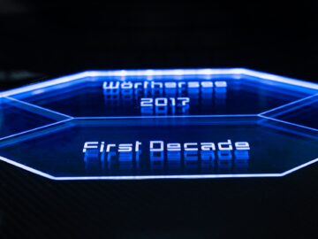 Close-up van een futuristisch blauw display met de tekst "Wörthersee 2017" en "First Decade" verlicht op een zeshoekige interface, waarop de iconische Volkswagen Golf te zien is.