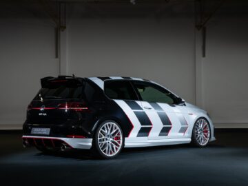 A black and white Volkswagen Golf GTI with red accents, displayed from the rear in a dimly lit environment, has a distinctive geometric pattern and striking red brake calipers.