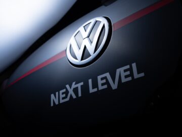 Volkswagen Golf-logo en de woorden "NEXT LEVEL" weergegeven op een donker oppervlak met een rode streep.