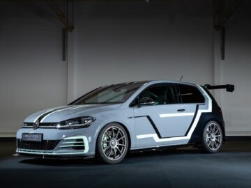 Ein modifizierter Volkswagen Golf GTI wird in einem schwach beleuchteten Raum ausgestellt, mit individuellen Grafiken, einem großen Heckflügel und Nachrüsträdern.