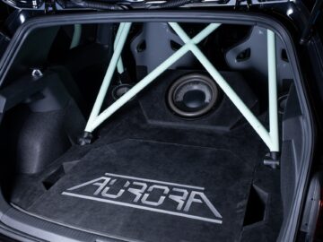 Ein Volkswagen Golf Kofferraum mit einem maßgeschneiderten Audio-Setup, einschließlich eines großen Subwoofers und grüner Stützbalken. Die Fußmatte trägt die Aufschrift 