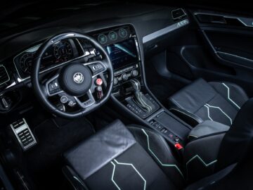 Interior view of a modern Volkswagen Golf with a leather-wrapped steering wheel, touchscreen display and leather seats with green accents. The dashboard includes several control buttons and digital gauges.