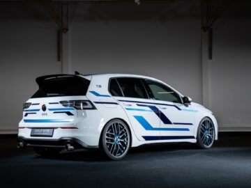 Im Inneren parkt ein weißer Volkswagen Golf GTE mit blauen geometrischen Emblemen. Der Volkswagen Golf ist mit maßgefertigten Felgen und einem Heckspoiler ausgestattet, die ihm einen schnittigen, modernen Look verleihen.