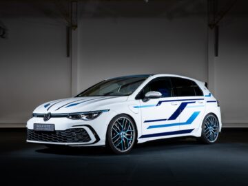 Een wit-blauwe Volkswagen Golf GTE hybride auto wordt tentoongesteld onder studioverlichting, wat het strakke ontwerp en de geavanceerde technologie benadrukt.