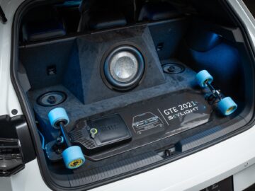 Shown is the trunk of a Volkswagen Golf containing a large subwoofer and two longboards. The trunk floor is labeled 