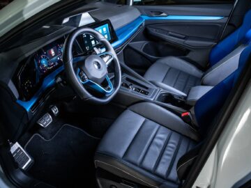 Interior of a modern Volkswagen Golf with a sleek black and blue leather design. The dashboard is equipped with digital displays and there is a multifunction steering wheel and center console.