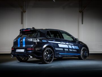 Inside, a black Volkswagen Golf GTE is parked, decorated with a blue and gray geometric pattern. The vehicle's taillights are illuminated and angled to highlight the rear and left side.