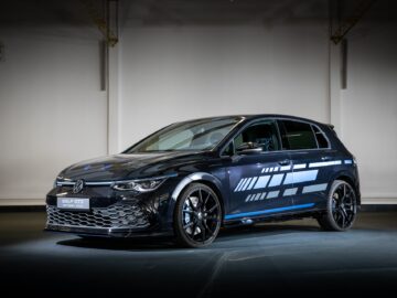 A Volkswagen Golf GTI in a showroom, with a dark blue exterior with striking white graphics on the side, illuminated under floodlights.