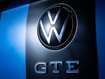 Close-up van een Volkswagen-logo boven de letters "GTE" op een blauw en zwart gestreept oppervlak, emblematisch voor het strakke ontwerp van de Volkswagen Golf.