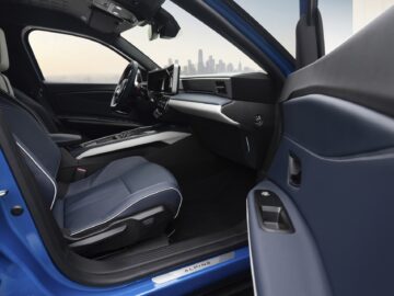 Binnenaanzicht van een moderne blauwe Renault 5 met leren stoelen, een digitaal dashboard en de skyline van de stad zichtbaar door de ramen.