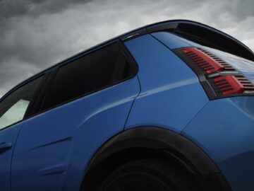 Close-up van het achterste gedeelte van een blauwe SUV met opvallende achterlichten, die doen denken aan het strakke ontwerp van een Alpine A290, tegen een bewolkte hemelachtergrond.