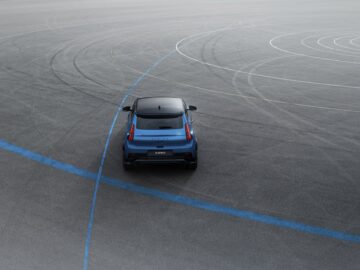 Een blauwe elektrische hot hatchback wordt van achteren vastgelegd op een asfaltoppervlak met cirkelvormige bandensporen.