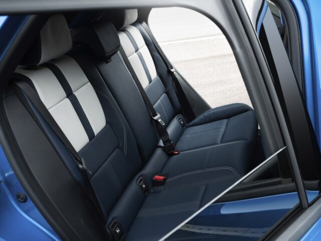 De afbeelding toont de achterbank van een Alpine A290 elektrische hot hatchback, voorzien van blauw-witte bekleding met veiligheidsgordels en hoofdsteunen. De deur aan de linkerkant staat open, waardoor er vrij zicht is op het zitgedeelte.