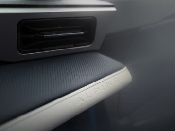 Close-up van een auto-interieur met een ventilatierooster en een deel van het dashboard met het woord "ALPINE" erop gedrukt, wat verwijst naar het verfijnde ontwerp van de Alpine A290 elektrische hot hatchback.
