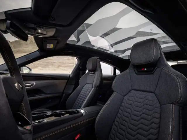 Binnenaanzicht van de Audi RS e-tron GT, met zwart gestoffeerde stoelen met stiksel en een panoramisch schuifdak, wat zijn indrukwekkende prestaties en luxe illustreert.