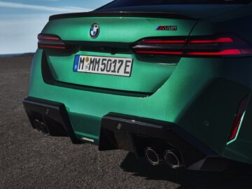 Primer plano de la parte trasera de un BMW M5 verde, mostrando las luces traseras, los tubos de escape cuádruples y la matrícula con un código alfanumérico.