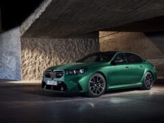 Een groene BMW M5 sedan staat geparkeerd in een slecht verlichte omgeving met betonnen muren.