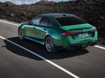 A green BMW sedan drives down a road with a mountainous landscape in the background.