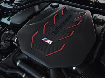 Close-up of an engine compartment, prominently showing the cover of a BMW M-series engine with decorative red accents and a central 