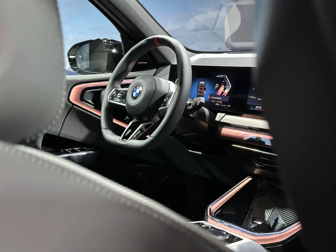 Vue de l'intérieur de la BMW X3 2024, avec le volant orné du logo emblématique de BMW et un tableau de bord numérique contenant diverses informations. Ce modèle souligne sa polyvalence et propose des moteurs à essence et diesel.