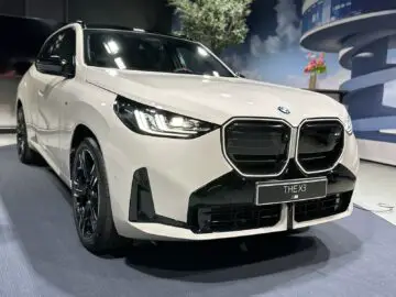 Ein weißer BMW X3 2024, der in einem Innenraum ausgestellt ist, von der vorderen linken Ecke aus gesehen, zeigt seine Dieselkraft.