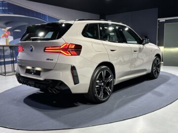 Une BMW X3 SUV blanche de 2024 est exposée à l'intérieur sur une plate-forme circulaire, avec l'arrière et le profil latéral visibles avec ses feux arrière éclairés distinctifs. Le véhicule est équipé de moteurs à essence et diesel, soulignant sa polyvalence et son ingénierie avancée.