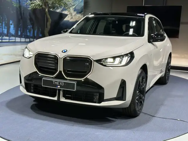 À l'intérieur, une BMW X3 est présentée sur une plateforme ronde, avec un design élégant comprenant des grilles distinctives, des phares à LED et des jantes noires. Cette beauté blanche allie luxe et puissance diesel pour une conduite exaltante.