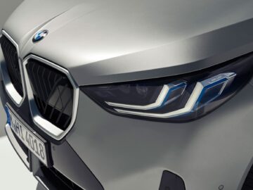 Gros plan sur la face avant d'une BMW X3 de 2024, mettant en évidence le phare et la calandre de gauche, avec le logo emblématique de BMW visible au-dessus. Le numéro d'immatriculation de la voiture est partiellement visible, montrant ses impressionnantes options essence et diesel.